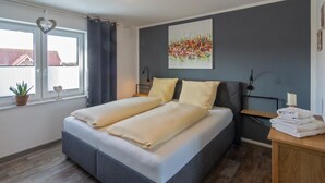 Un dormitorio con una cama, una ventana, una planta y un cuadro en la pared.