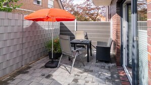 Un patio con una mesa, sillas, una planta en maceta y un paraguas naranja.