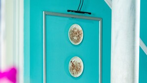Una obra de arte enmarcada sobre una pared turquesa, un pilar blanco y un suelo a cuadros.