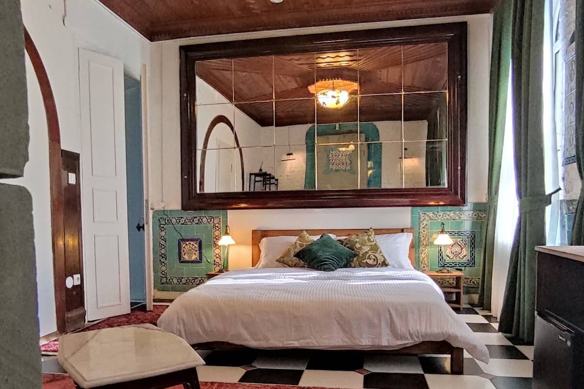 A bedroom with a bed, a nightstand, a chair, a mirror, and a chandelier.