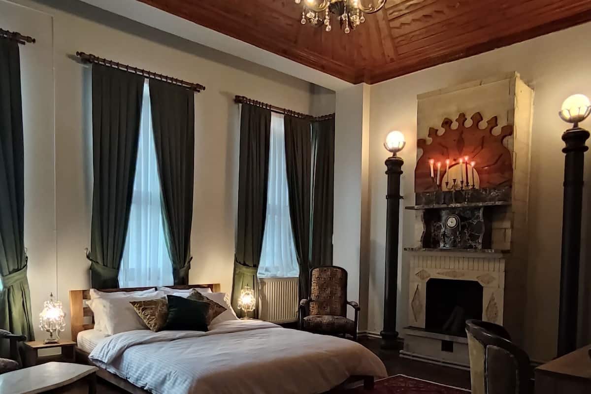 A bedroom with a large bed, a red patterned rug, a fireplace, and a wooden ceiling.