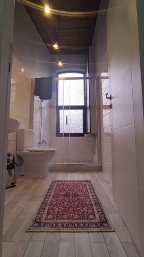 A bathroom with a shower, toilet, and sink, a patterned rug on the floor, and a window with a stained glass design. - Nevalist Hotel (Istanbul)