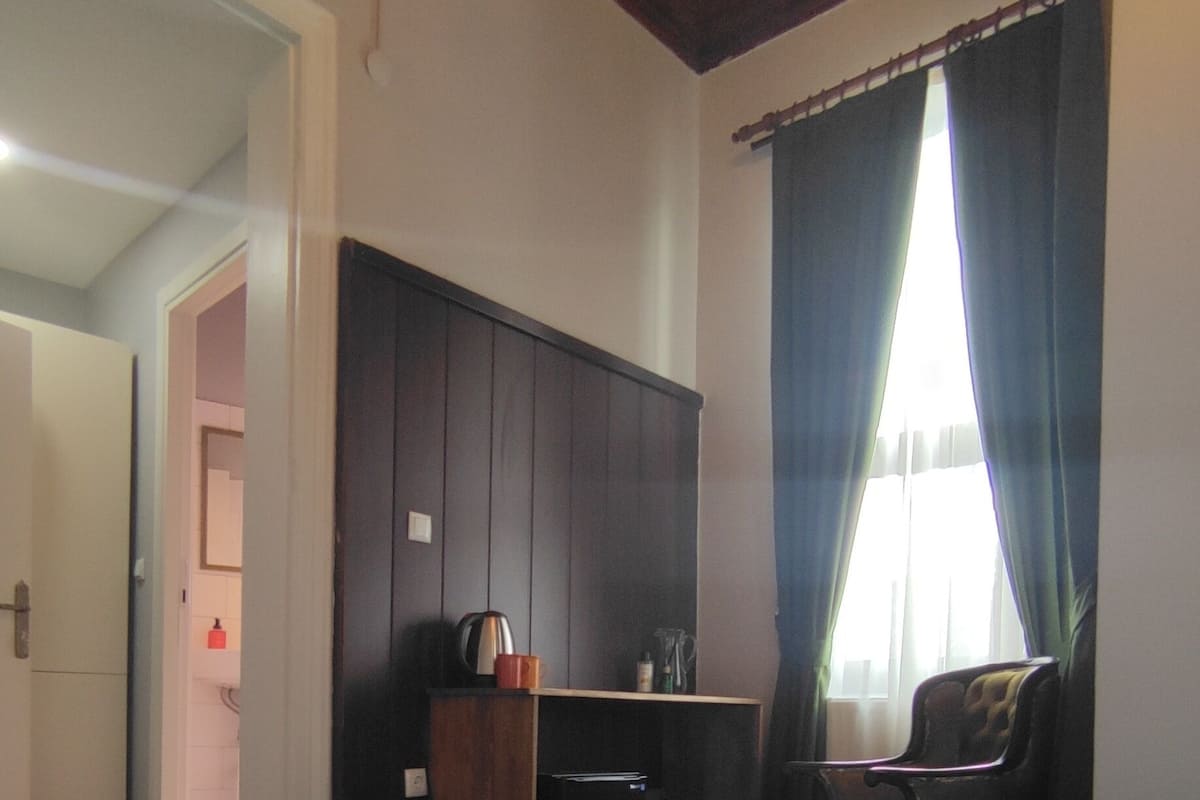 A hotel room with a large bed, a desk, a chair, and a wardrobe.