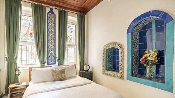 Un dormitorio con cama, mesita de noche, lámpara y ventana con cortinas verdes.