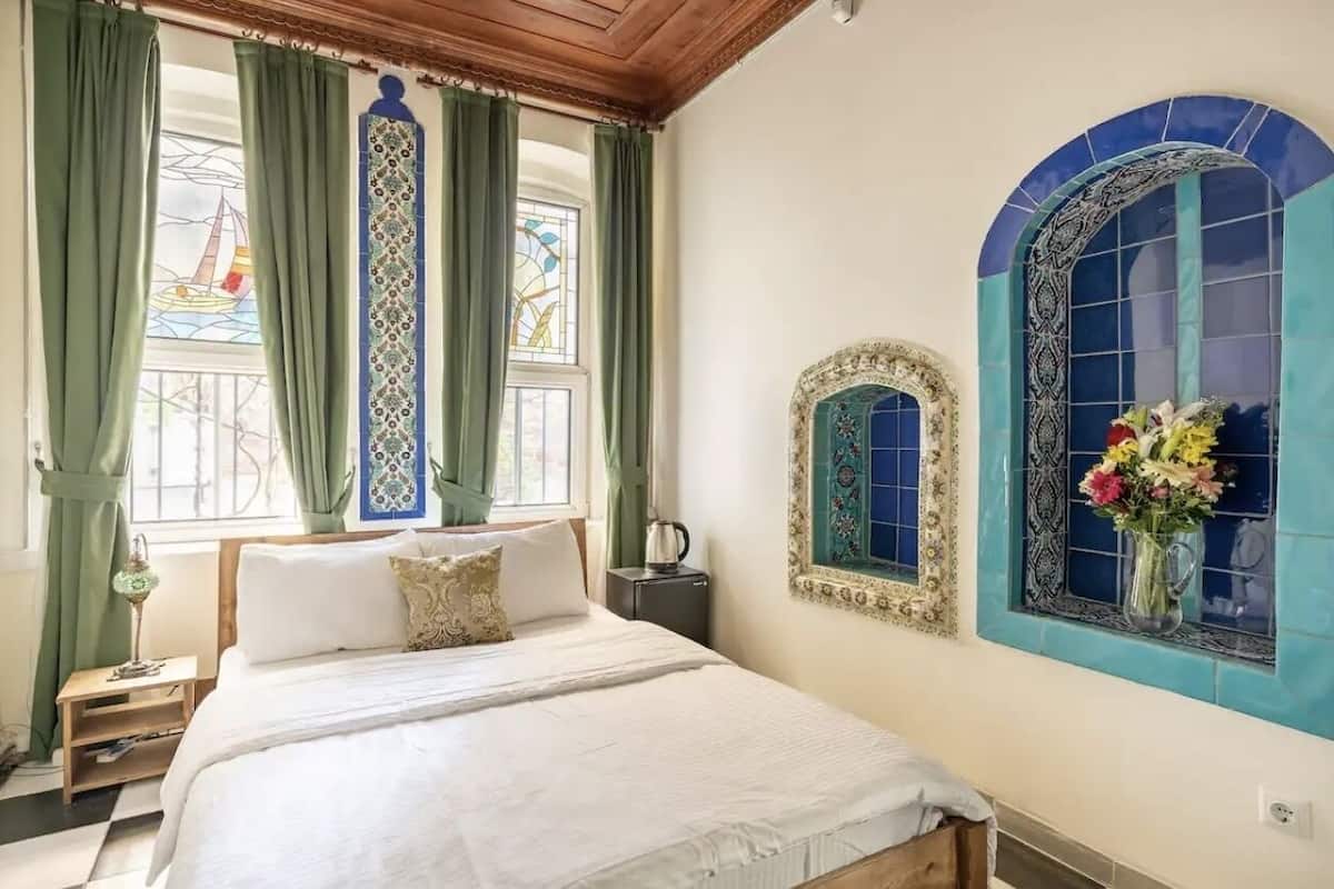 A bedroom with a bed, a nightstand, a lamp, and a window with green curtains.