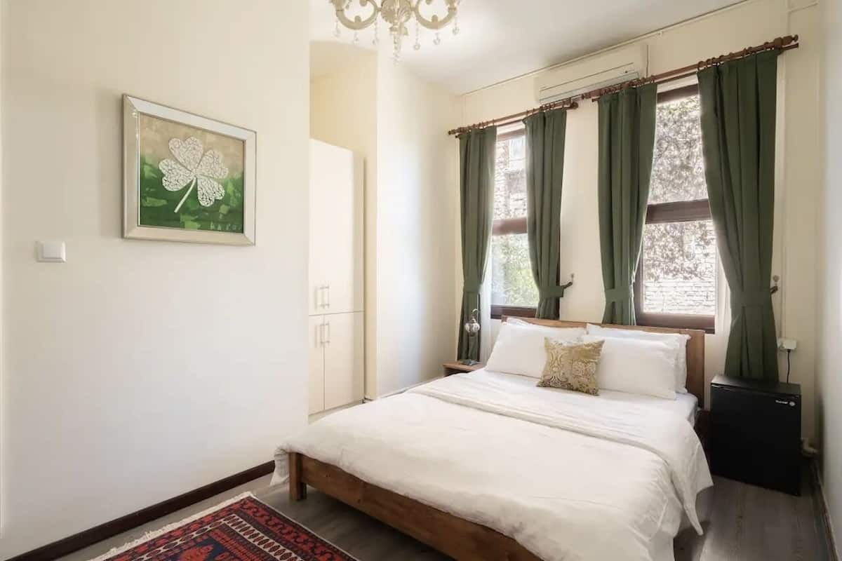 A bedroom with a bed, a nightstand, a dresser, a chandelier, and a window with curtains.