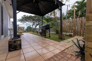 A covered patio area with a grill, seating, and a wooden fence.