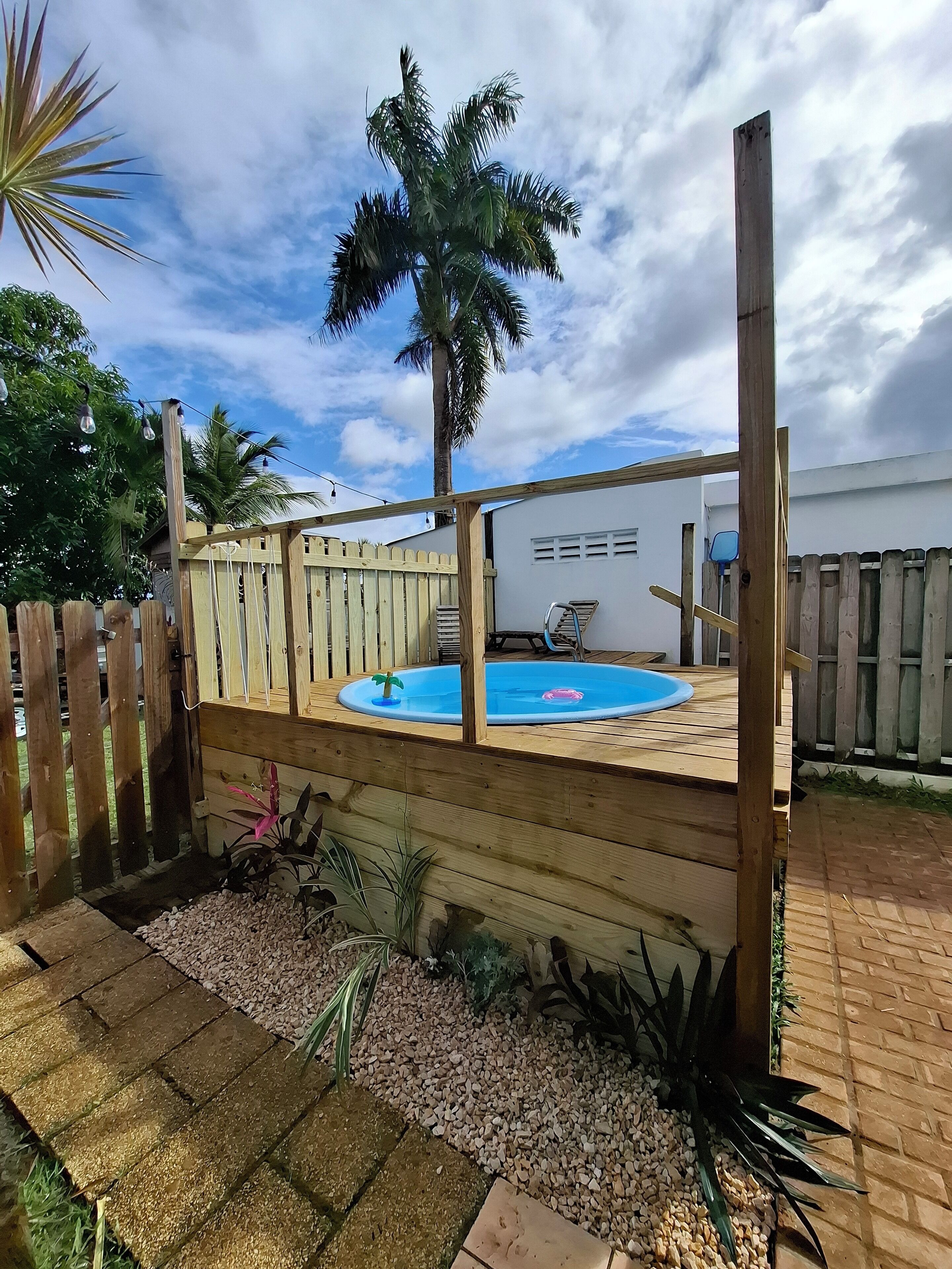 Eine Holzterrasse mit Schwimmbecken, umgeben von einem Holzzaun und Palmen.