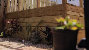 Een houten terras met een witte hek, omringd door potplanten en een palmboom.