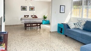 Een woonkamer met een blauwe bank, een eettafel met stoelen, een plafondventilator en ingekaderde foto's aan de muren.