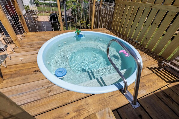 A hot tub on a wooden deck with a metal ladder and a pink flamingo float.