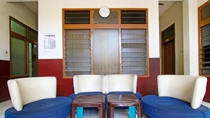 A waiting area with a sofa and two small tables, a clock, and a wall with a list of names and numbers. - Hotel O Mutiara (Magelang)