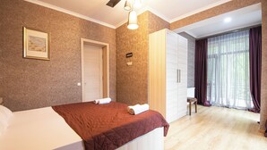 Quarto de hotel com cama, guarda-roupa, espelho e janela com cortinas.