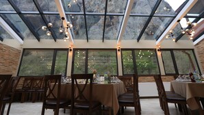 Um restaurante com teto de vidro, cadeiras e mesas de madeira preparadas para refeições.
