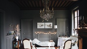 A room with a chandelier, a bed, two chairs, a table with a lamp, and artwork on the wall. - Roomshala 111 Cosy Nook (New Delhi)