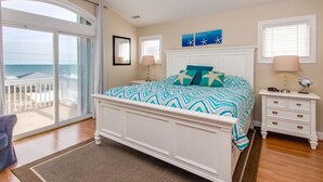 Een slaapkamer met een groot bed, een nachtkastje, een stoel en uitzicht op de oceaan door een schuifdeur.