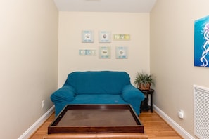 A living room with a blue sofa, a wooden coffee table, and wall art including a 'BEACH' sign and framed pictures. - Sol Mate - 5BR 2nd Row Home with Ocean Views, Pool, Hot Tub & Pet Friendly! (North Topsail Beach)