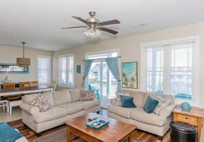 A living room with two sofas, a wooden coffee table, a ceiling fan, and a dining area with a table and chairs.