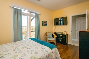 A bedroom with a bed, a dresser, a chair, a television, and a door leading to another room. - Sol Mate - 5BR 2nd Row Home with Ocean Views, Pool, Hot Tub & Pet Friendly! (North Topsail Beach)