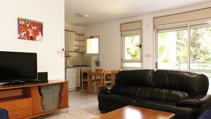 Un salon avec un canapé en cuir noir, une table basse en bois, un téléviseur posé sur un meuble en bois, et un coin repas comprenant une table et des chaises.