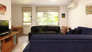 Un salon avec un canapé en cuir noir, un meuble TV en bois et un coin repas comprenant une table et des chaises.