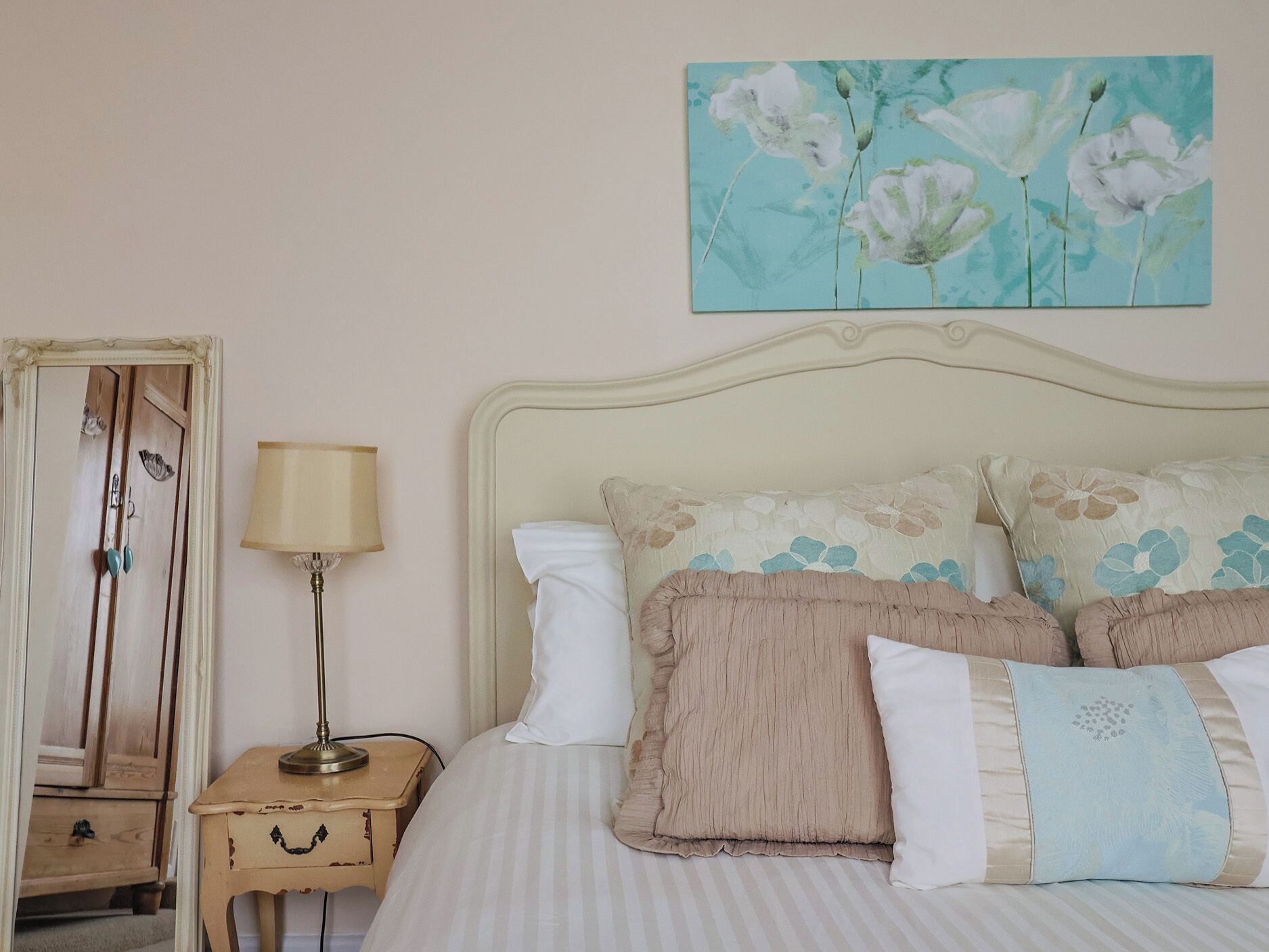 A bedroom with a bed, bedside table, lamp, and a floral painting on the wall.