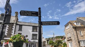 Placa de rua com indicações para serviços locais, incluindo lojas, pubs, cafés e o caminho costeiro.
