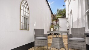 Un patio con mobiliario de mimbre, una mesa y un ventanal decorativo.
