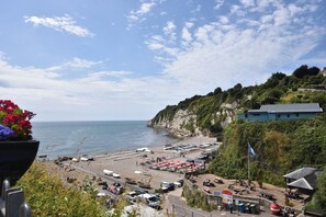 A coastal beach area with a paved walkway, umbrellas, and a flagpole. - Apartment 1, Durham House (Seaton)