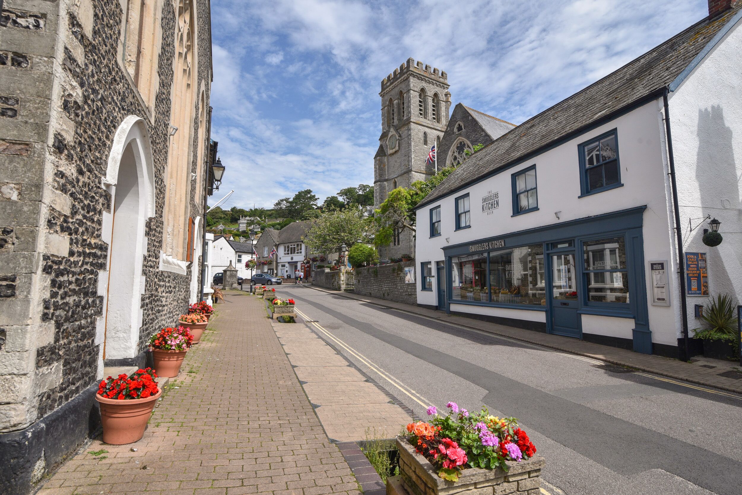 A street with historic buildings, a church, and flower-lined sidewalks.