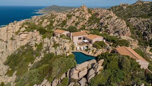 Una villa costera con piscina, rodeada de terreno rocoso y vegetación.