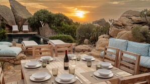 Una mesa dispuesta para comer con vista al atardecer, rodeada de formaciones rocosas y vegetación.