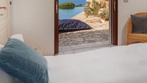 Un dormitorio con cama, televisión, una silla de mimbre y vistas a la playa y al mar.