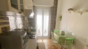 Une cuisine compacte équipée d’un four à micro-ondes, d’une cuisinière et d’un évier. On y trouve une table à manger avec des chaises, et une porte vitrée donne sur un balcon.