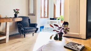 Una sala de estar con piso de madera, un sillón estampado, una mesa blanca y una planta en maceta.