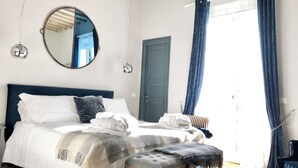 Un dormitorio con cama, un espejo redondo, una puerta y un ventanal con cortinas.