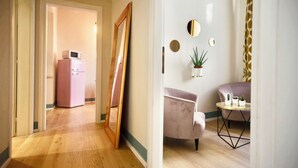 Un pasillo con un refrigerador rosa, un espejo, una silla y una mesita con plantas.