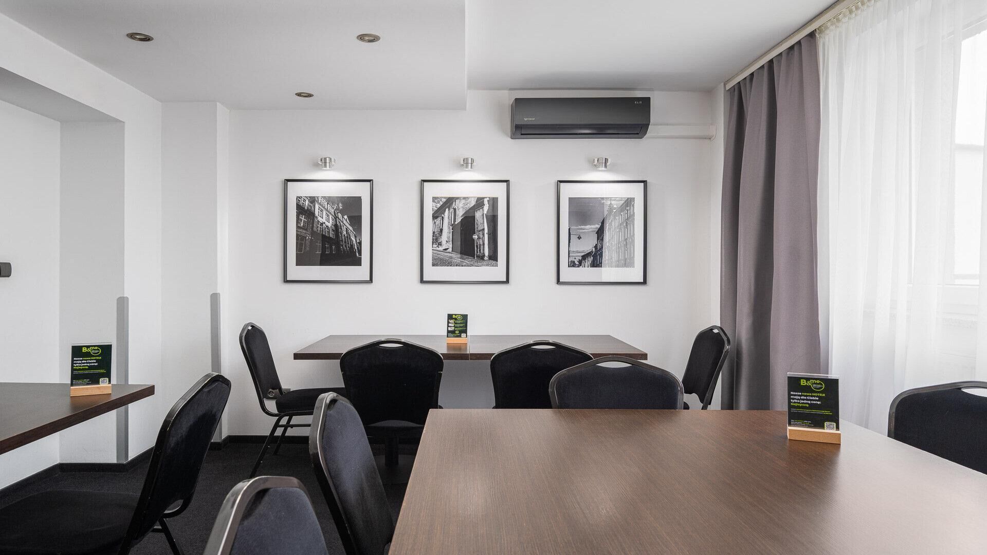 Una sala de conferencias con una mesa de madera, sillas negras y tres fotografías en blanco y negro enmarcadas en la pared.