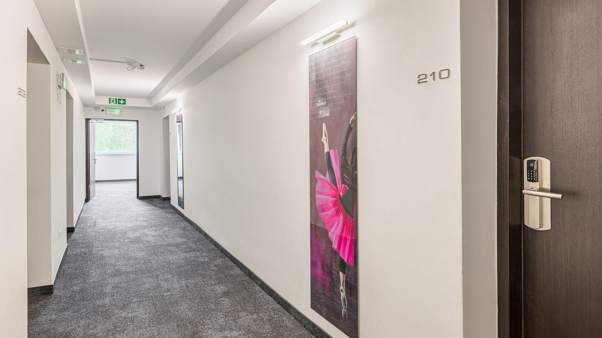 Un pasillo con piso alfombrado, una puerta con cerradura electrónica y un cartel en la pared.