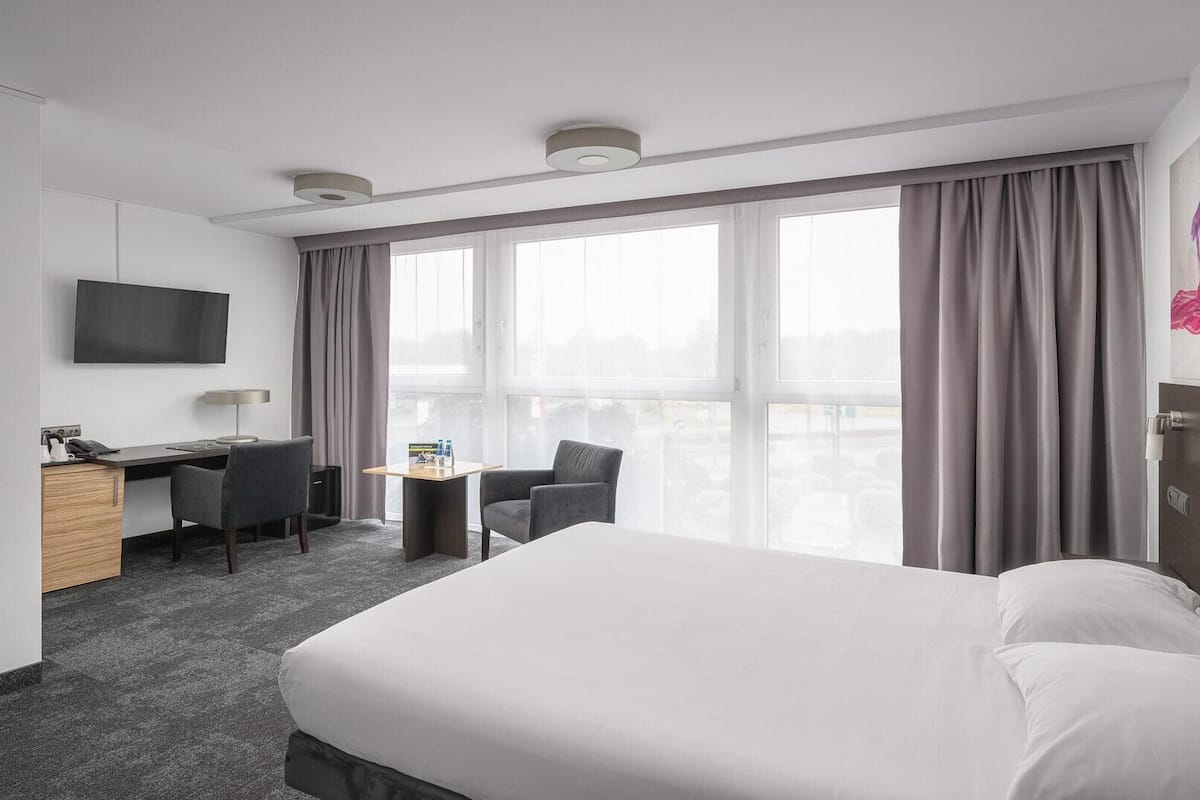 A hotel room with a large bed, a desk with a chair, a television, and a window with curtains.