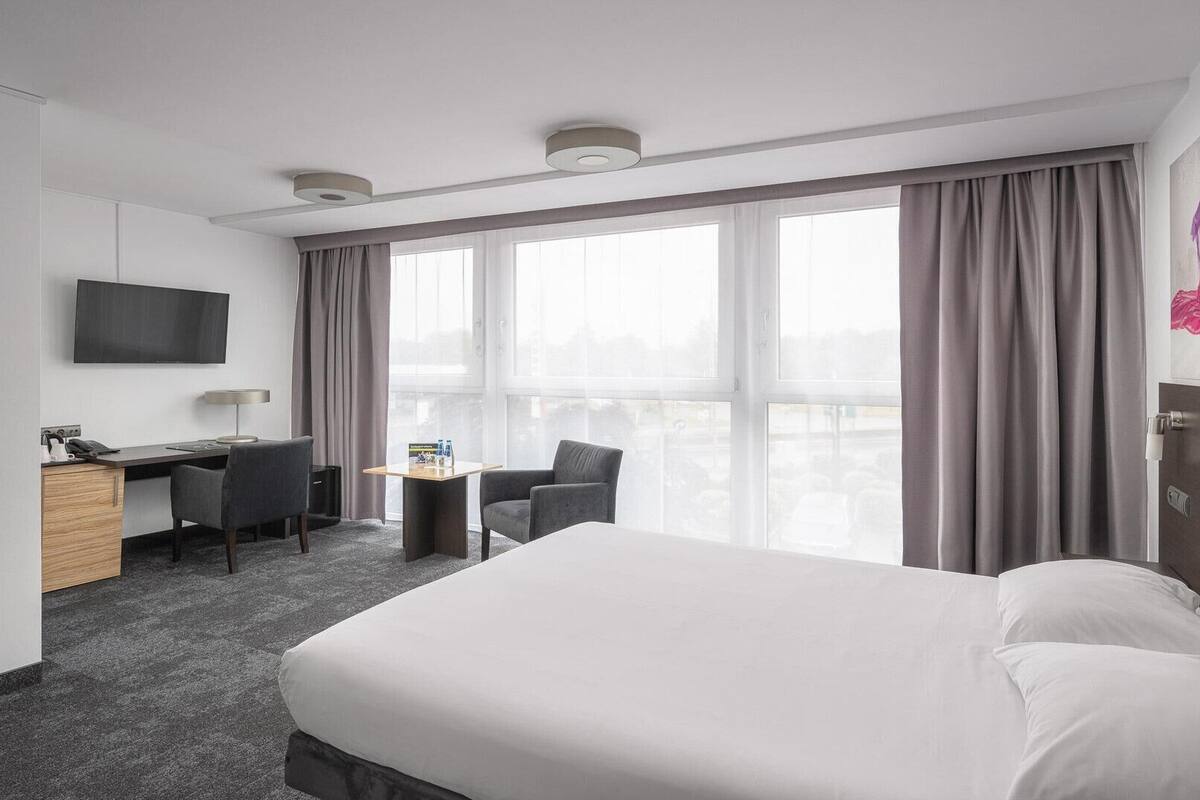 Hotellihuone, jossa on suuri sänky, työpöytä tuolilla, televisio ja ikkuna, jossa on verhot.
