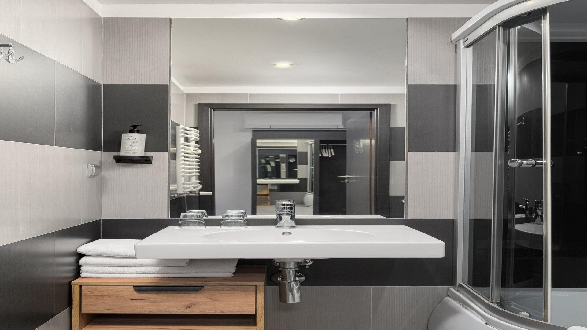 Un baño moderno con un espejo grande, dos lavamanos, una ducha y un armario de madera.
