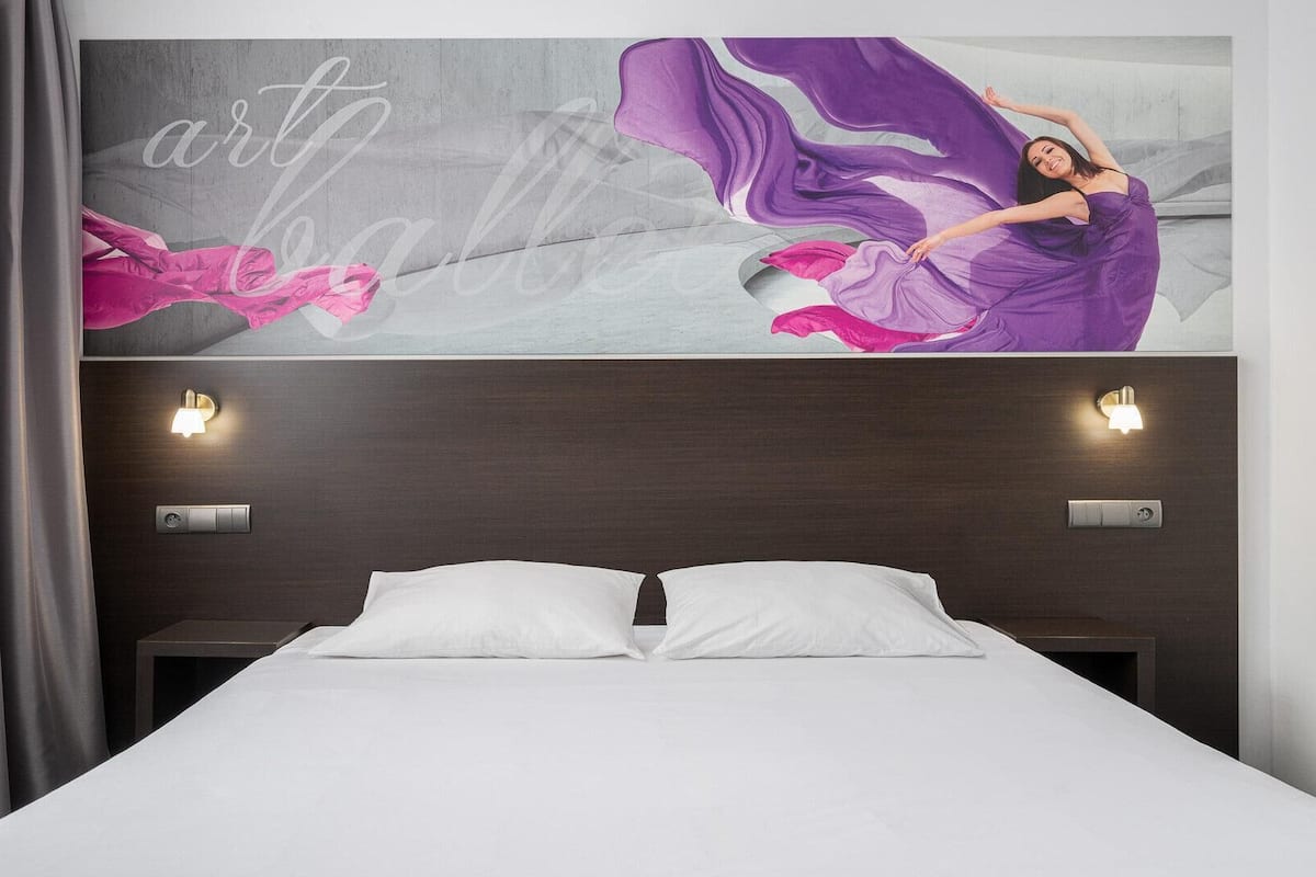 A modern hotel room with a large bed, two bedside tables, and a wall-mounted light fixture.