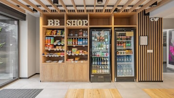 Uma loja BB com prateleiras de madeira repletas de lanches e bebidas, e duas vitrines refrigeradas.