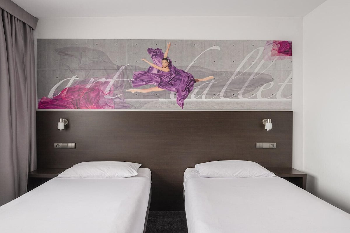 A hotel room with two single beds, a large abstract painting on the wall, and a modern design.