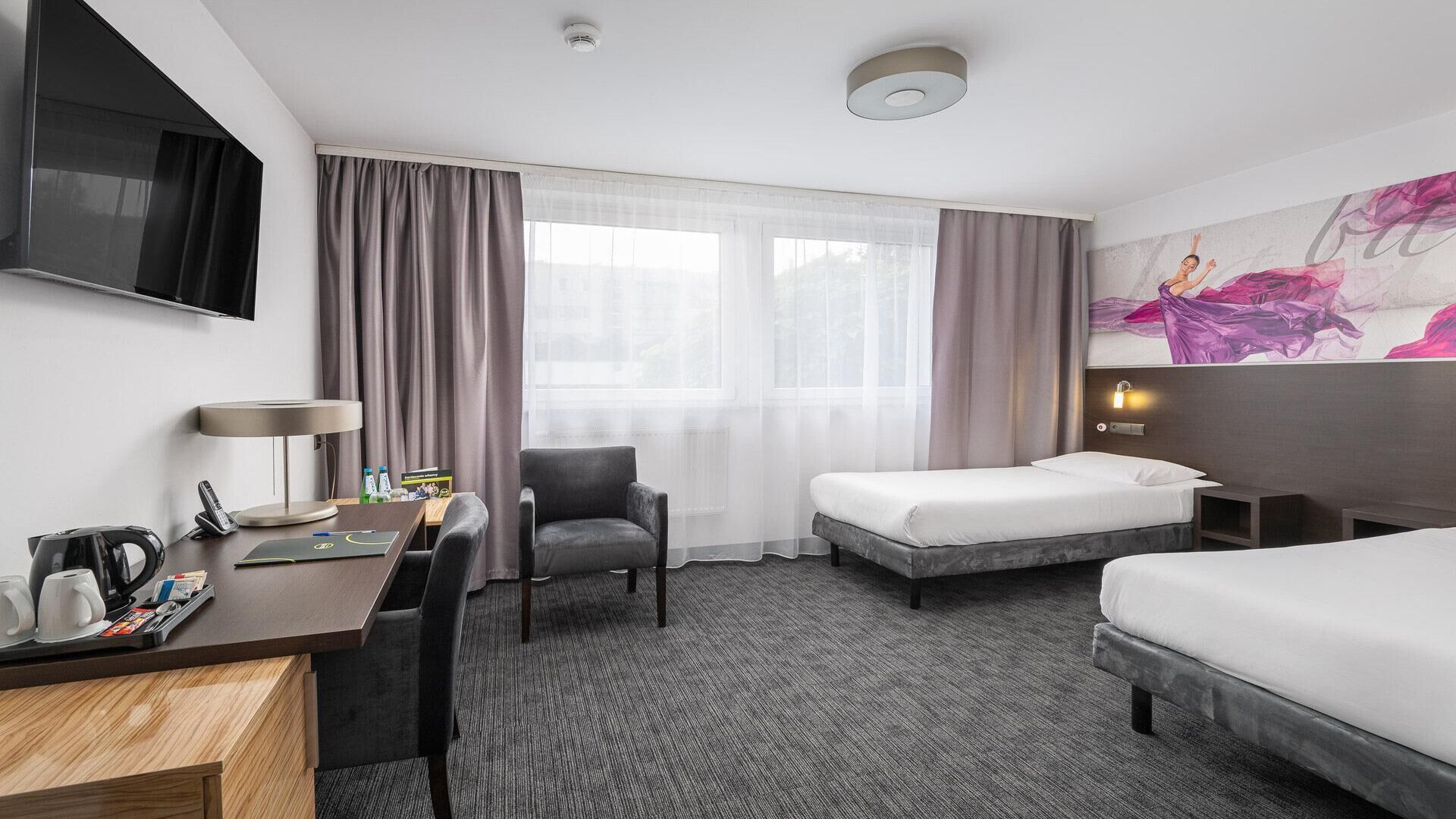 Habitación de hotel con escritorio, silla, dos camas, televisión y un cuadro en la pared.
