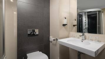 Un baño moderno con un lavamanos blanco, una cabina de ducha de vidrio y un espejo sobre el lavamanos.