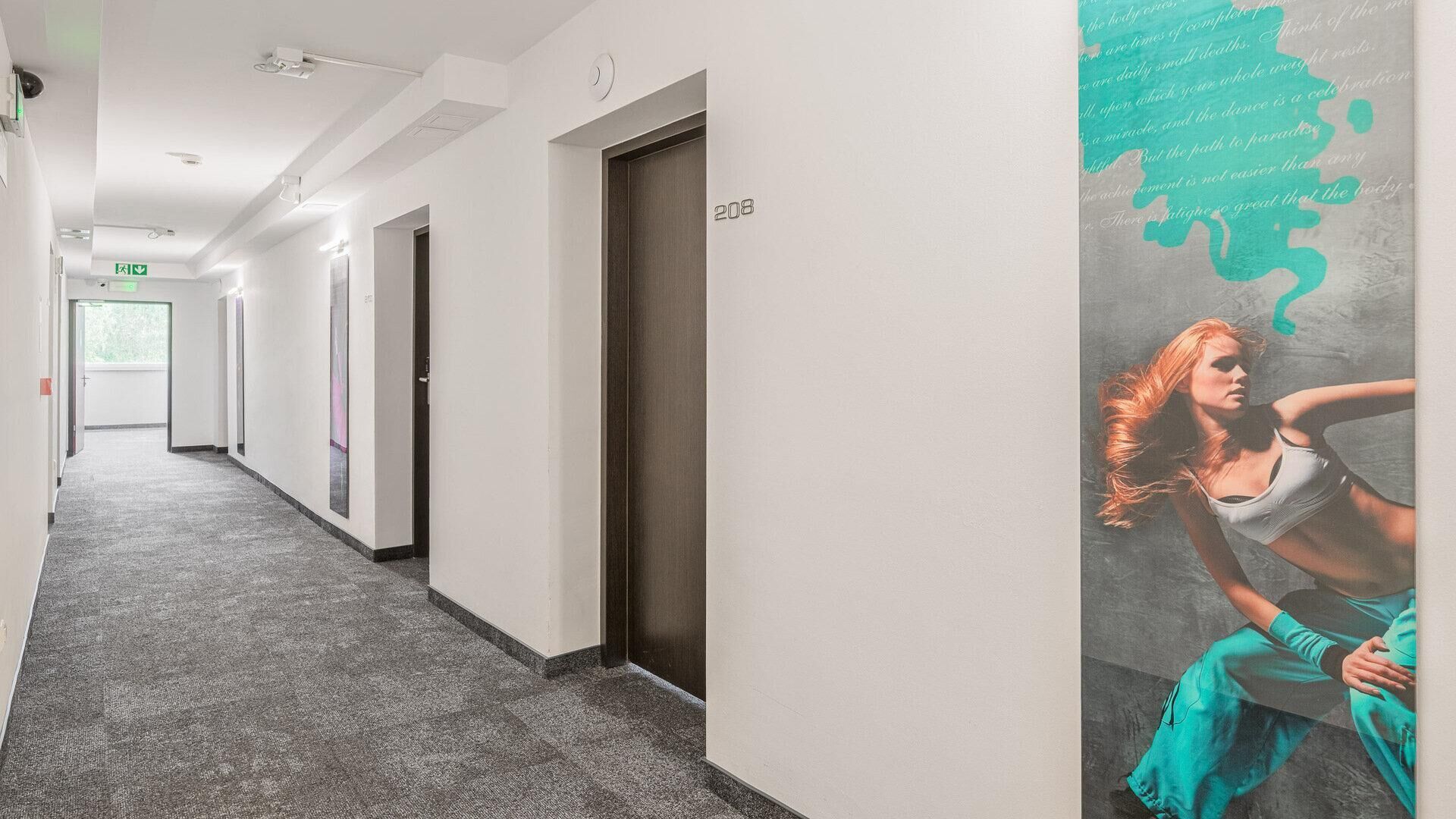 Un pasillo de hotel con piso alfombrado, puertas numeradas 208 y un mural en la pared.