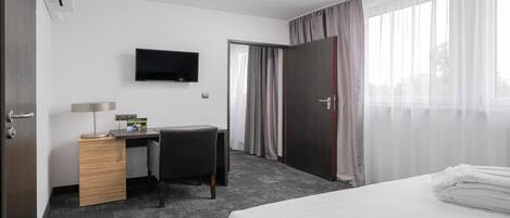 Habitación de hotel con cama, escritorio, silla, televisor y puerta con cortinas.