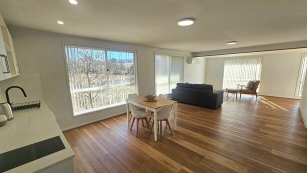 A spacious living area with a dining table and chairs, a sofa, and a balcony with a view. - Guest Suite Bredbo (Jerangle)